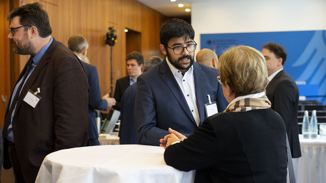 Frauen und Männer stehen an Stehtischen und unterhalten sich. (Quelle: © Annalena Sippl) Frauen und Männer stehen an Stehtischen und unterhalten sich.