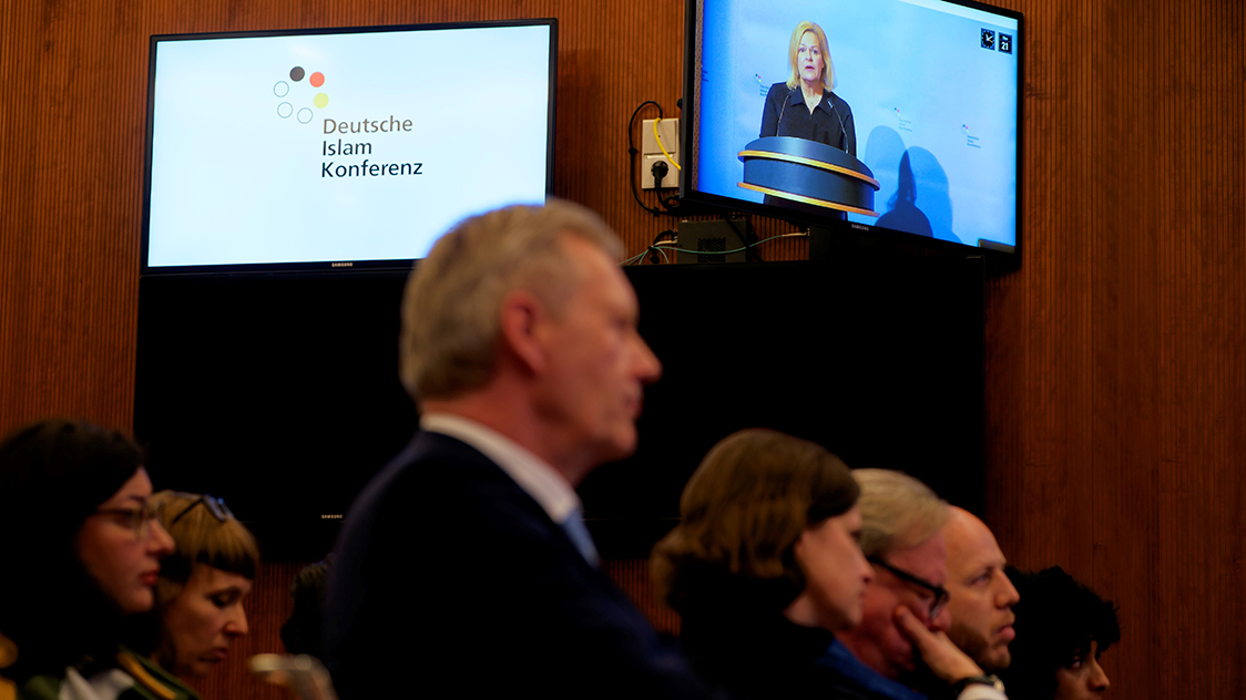 Frauen und Männer sitzen auf Stuhlreihen. Zwei kleine Bildschirme befinden sich im Hintergrund.  (Quelle: © Henning Schacht) Frauen und Männer sitzen auf Stuhlreihen. Zwei kleine Bildschirme befinden sich im Hintergrund.