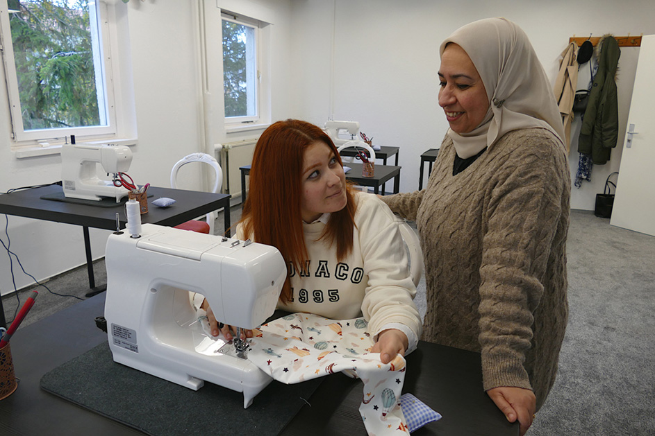 Eine Frau sitzt und eine Frau steht vor einer Nähmaschine.  (Quelle: Stop press & public/Helmut Stapel) Eine Frau sitzt und eine Frau steht vor einer Nähmaschine.