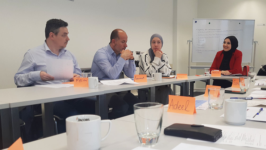 Frauen und Männer sitzen an Tischen, die in einer U-Form aufgestellt sind. (Quelle: Claudia Mende) Frauen und Männer sitzen an Tischen, die in einer U-Form aufgestellt sind.