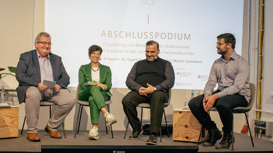 Vier Person sitzen in einem Halbkreis auf einer Bühne (Quelle: Syspons GmbH) Vier Person sitzen in einem Halbkreis auf einer Bühne