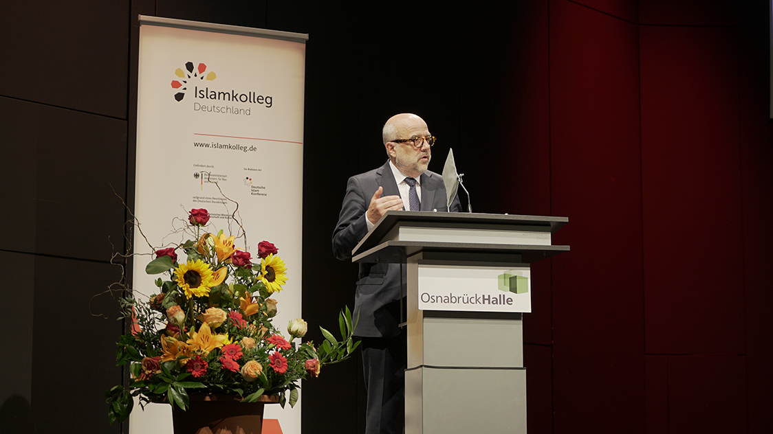 Ein Mann steht vor einem Rednerpult (Source: Islamkolleg Deutschland e.V.) Ein Mann steht vor einem Rednerpult